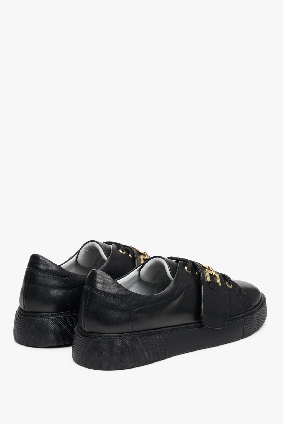Women's black leather sneakers by Estro with a gold embellishment - close-up on the heel and side seam of the shoes.