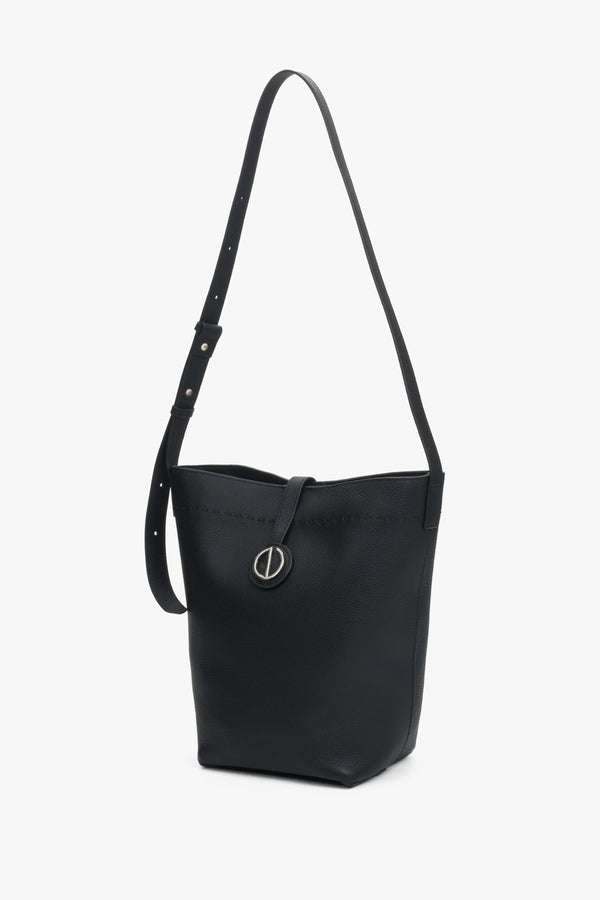 Side profile of a women's black leather bucket bag, showing its cylindrical shape and strap.