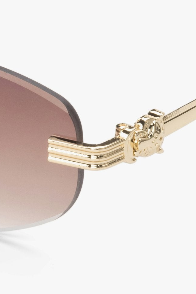 A pair of oval, frameless sunglasses with brown lenses and gold hardware.