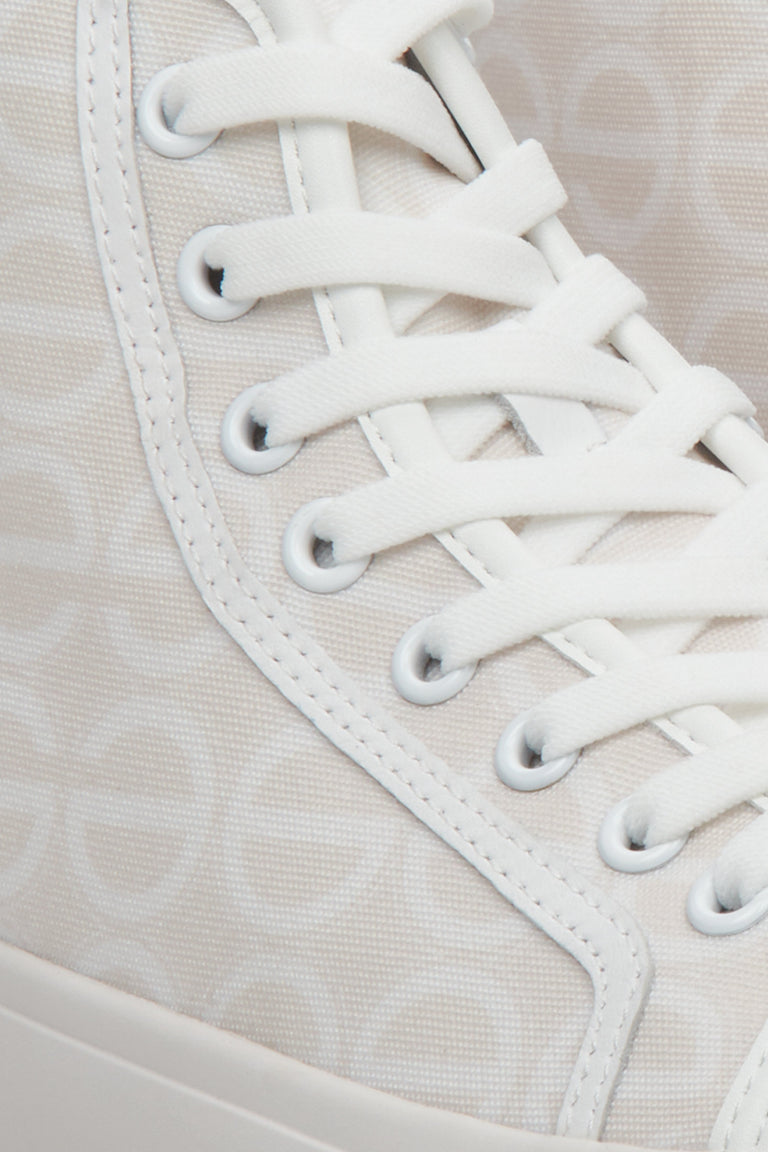 Sporty women's sneakers in beige and white, laced - a close-up on details.