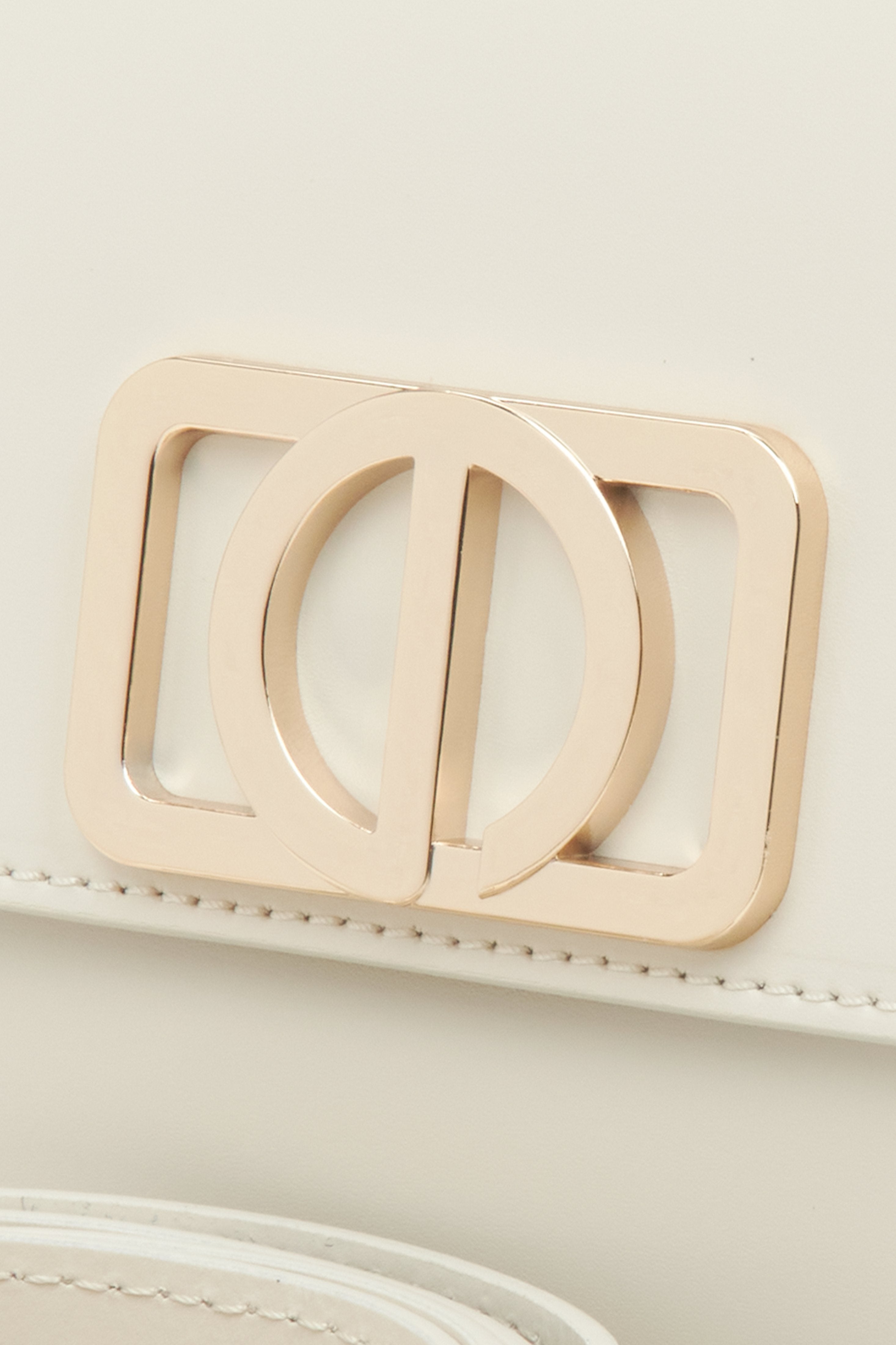 Feminine handbag in milky-beige, compact in size, in the baguette style - close-up on the detail.