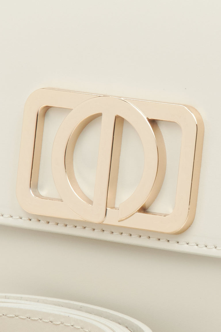 Feminine handbag in milky-beige, compact in size, in the baguette style - close-up on the detail.