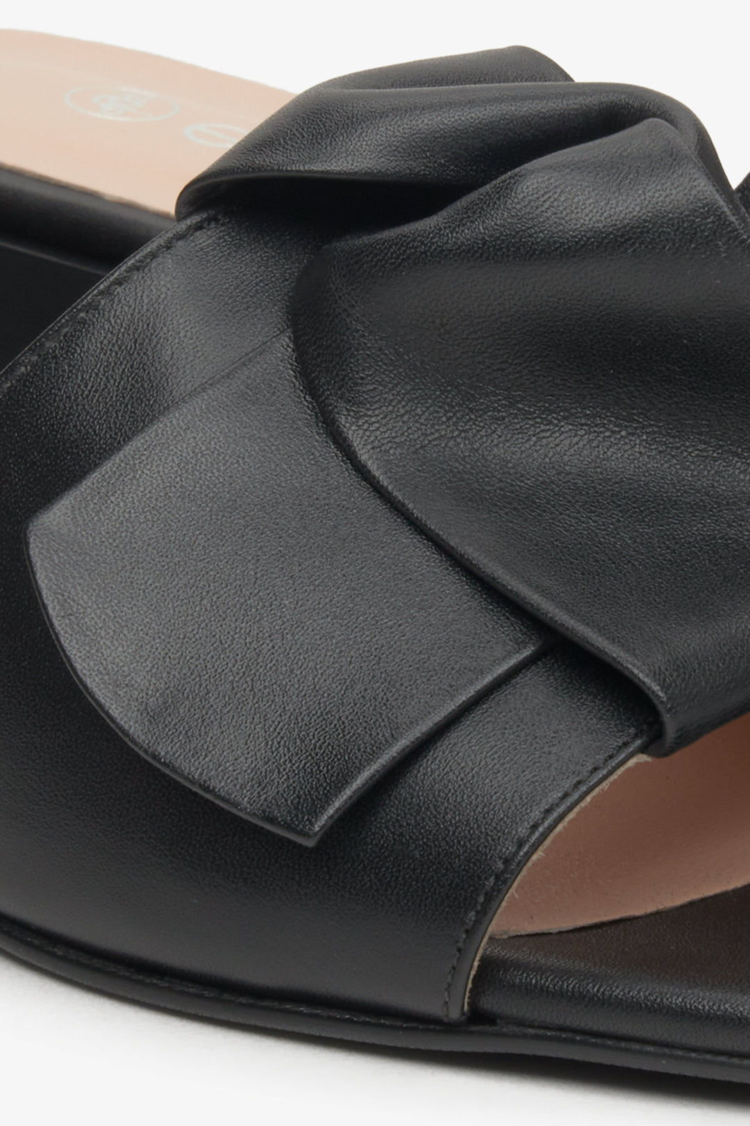 Women's black leather  mules by Estro with a decorative bow - close-up on the ornament.