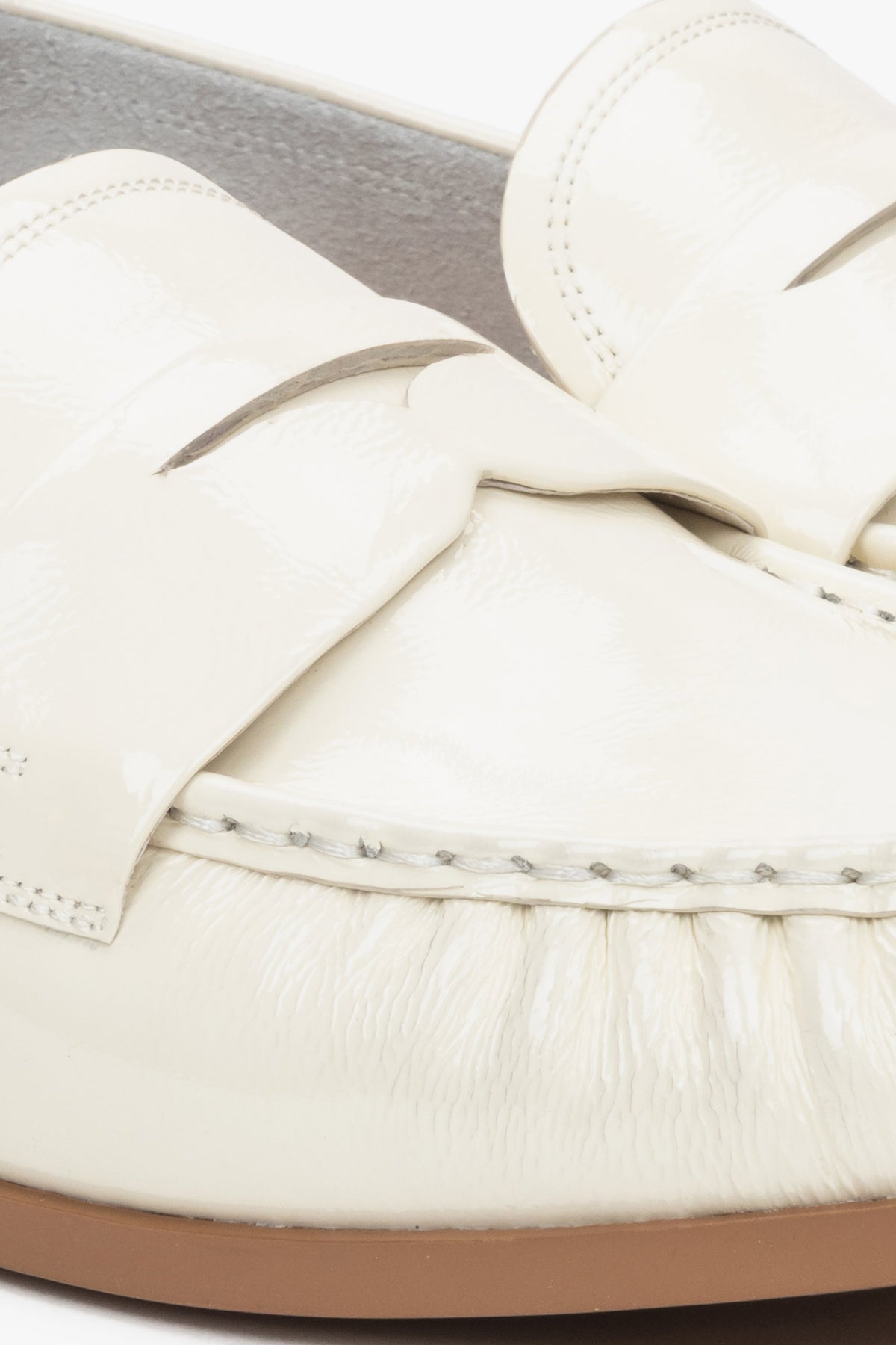 Stylish women's loafers made of white patent genuine leather – close-up on the details.

