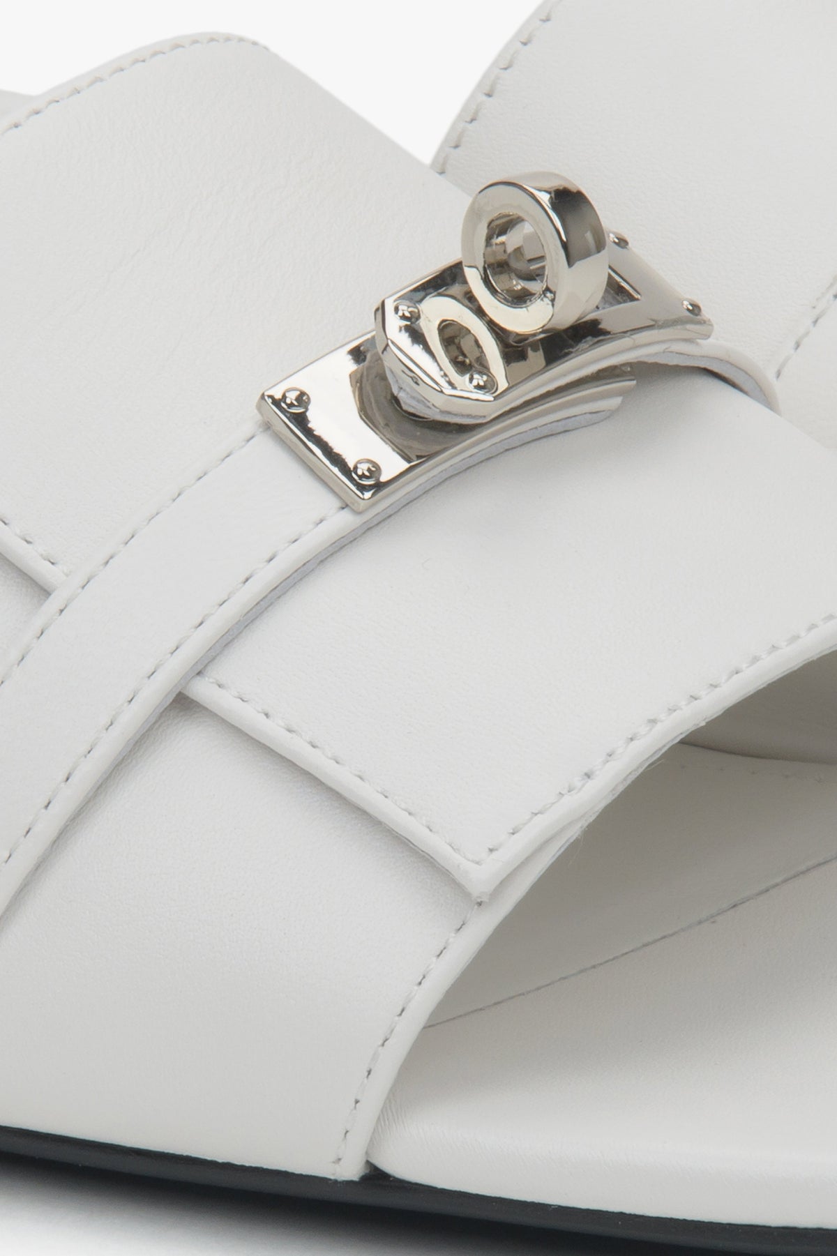White flat-heeled slides with a silver embellishment from Estro – a blend of comfort, subtle elegance, and versatile design, close-up on details.