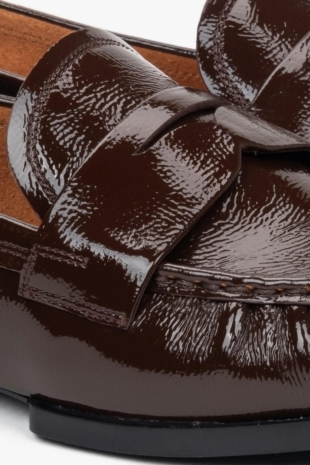 Stylish women's loafers made of dark brown patent genuine leather – close-up on the details.