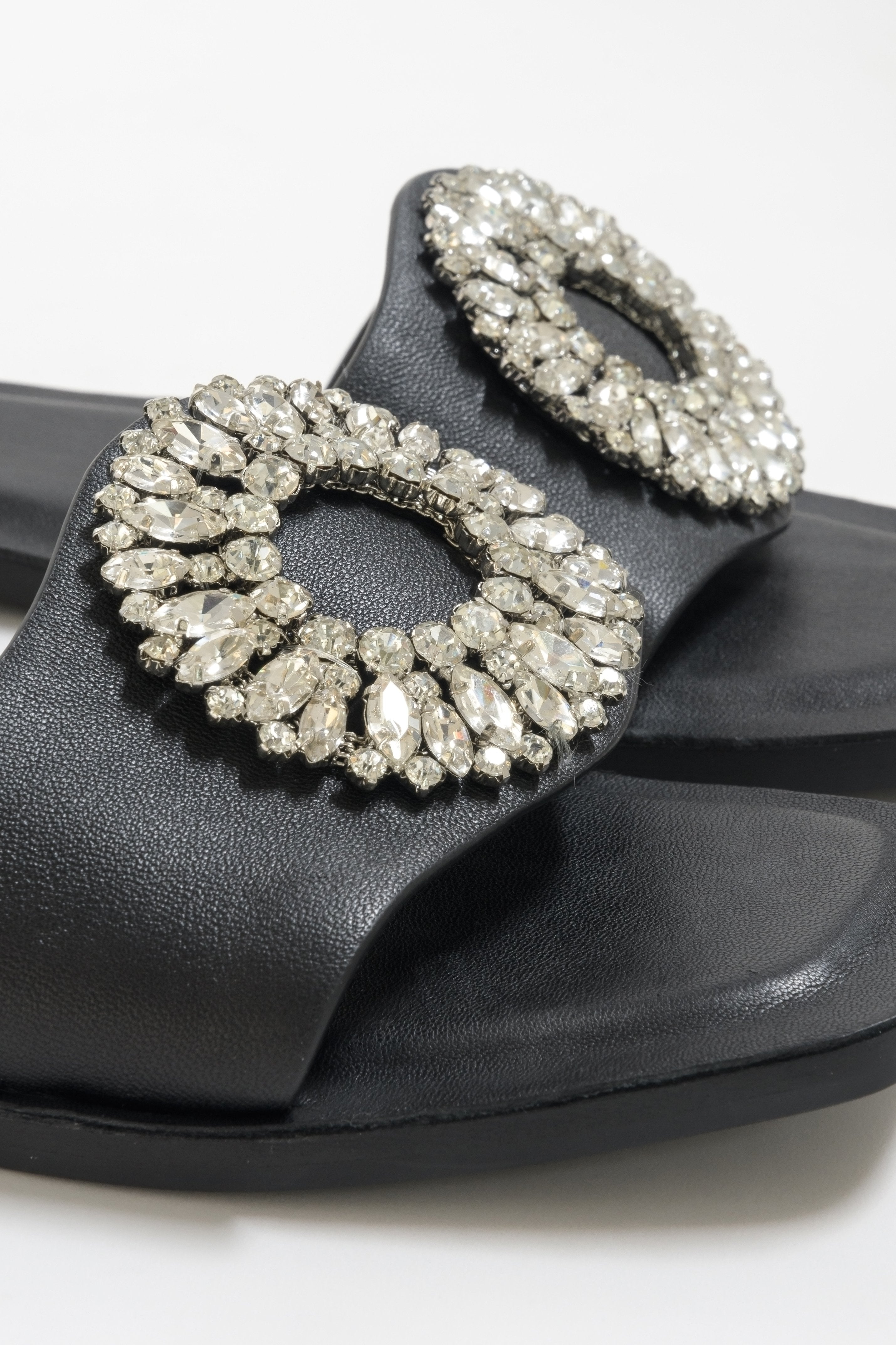 Flat slide sandals made of genuine leather in black - close-up on zirconias ornament.