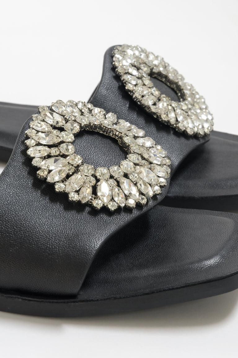 Flat slide sandals made of genuine leather in black - close-up on zirconias ornament.