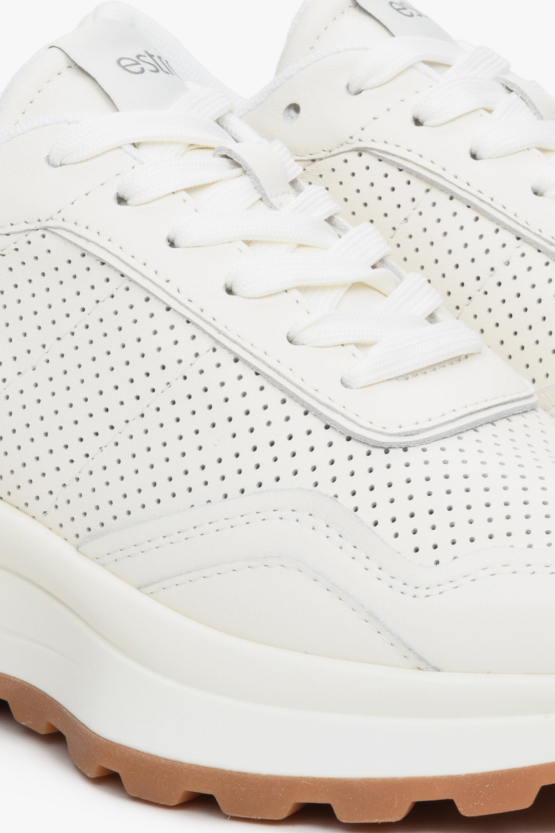 Women's white leather sneakers with perforation - close-up of the stitching pattern.