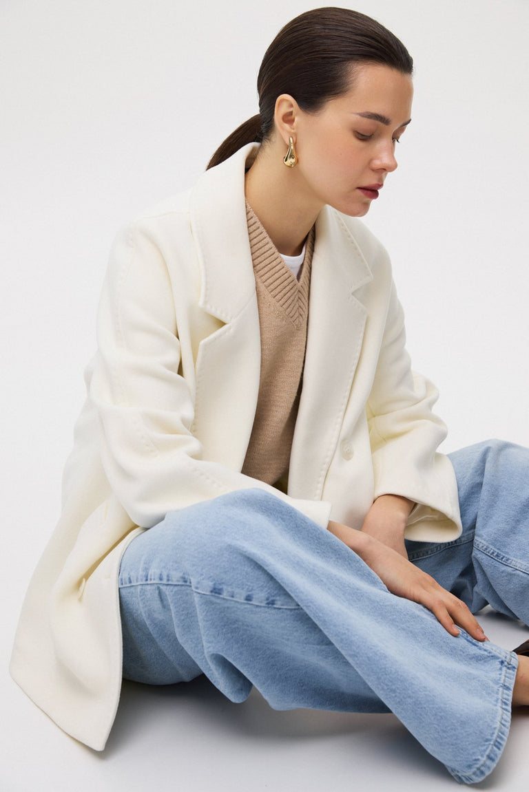 A short, white, double-breasted women's coat made of wool by Estro.