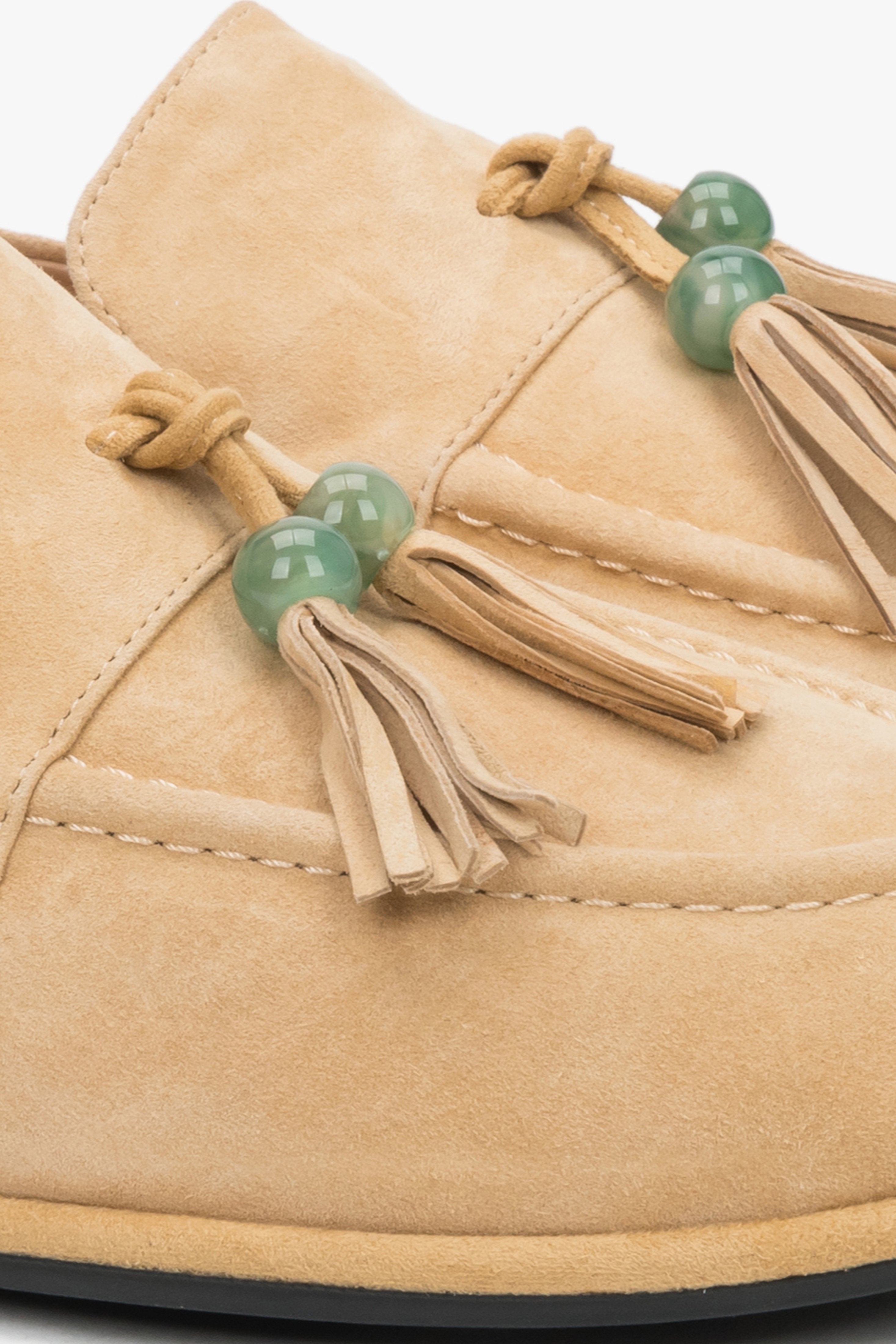 A close-up shot of the front of the shoe, displaying the artisanal decorative tassel with a green bead and the soft, matte texture of the light suede.
