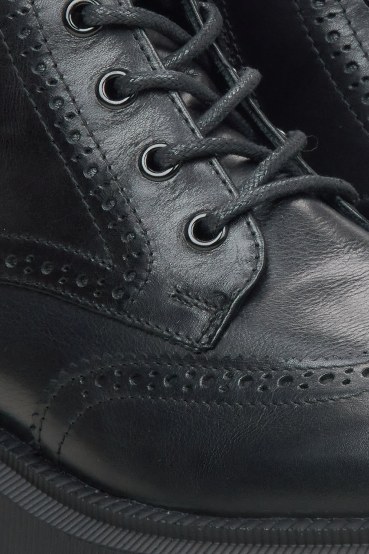 Close-up of a black leather lace-up boot with brogue perforated detailing and dark laces.