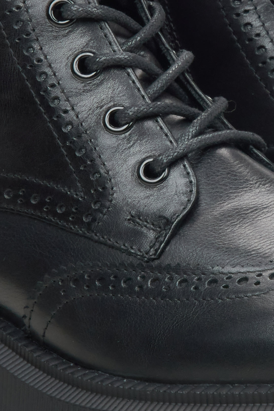 Close-up of a black leather lace-up boot with brogue perforated detailing and dark laces.