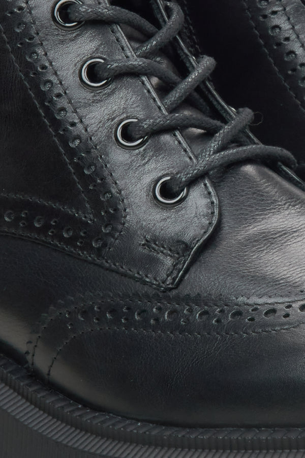 Close-up of a black leather lace-up boot with brogue perforated detailing and dark laces.