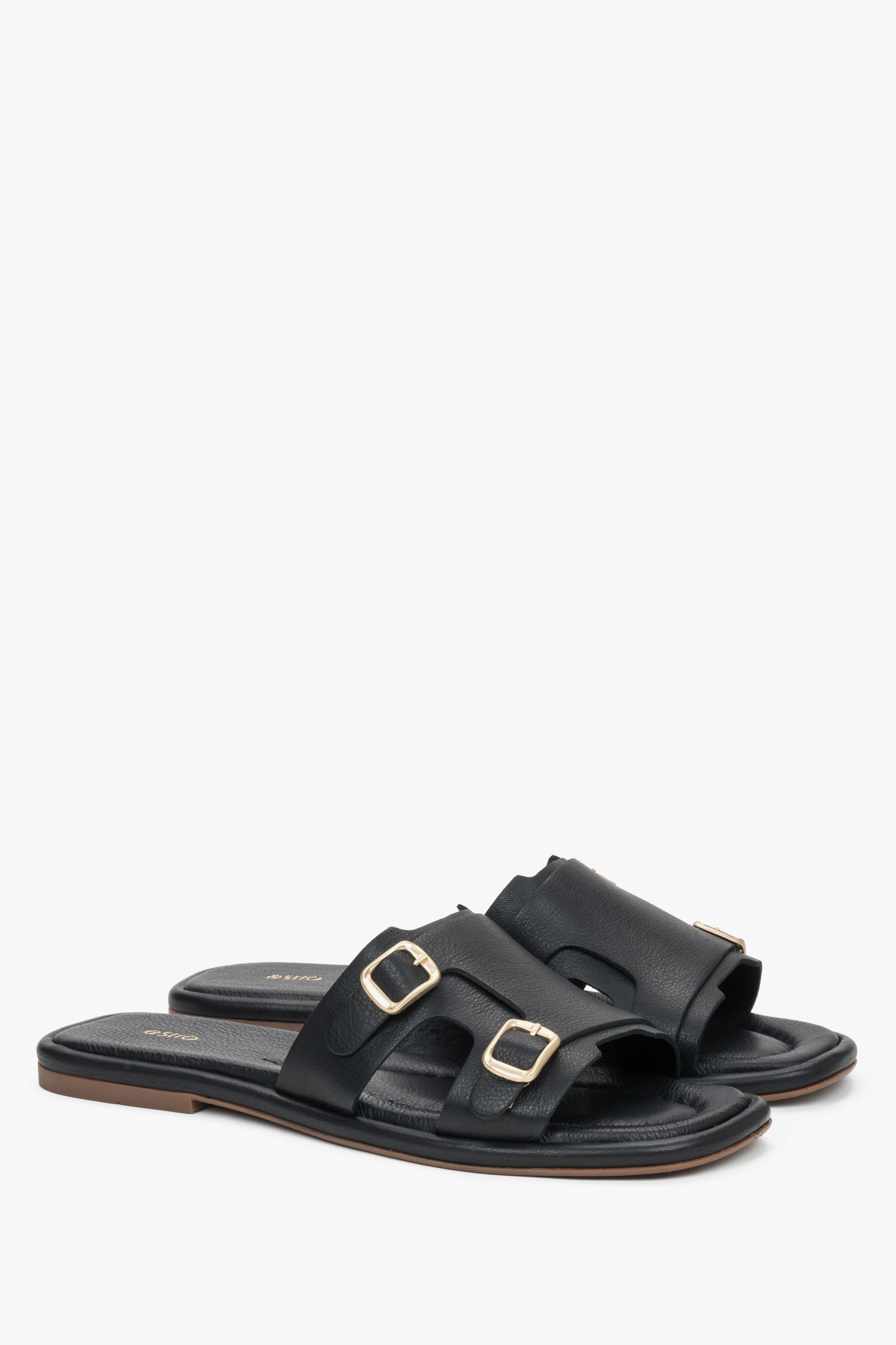 A close-up shot focusing on the smooth, deep black leather texture and the polished brilliance of the adjustable golden buckles.