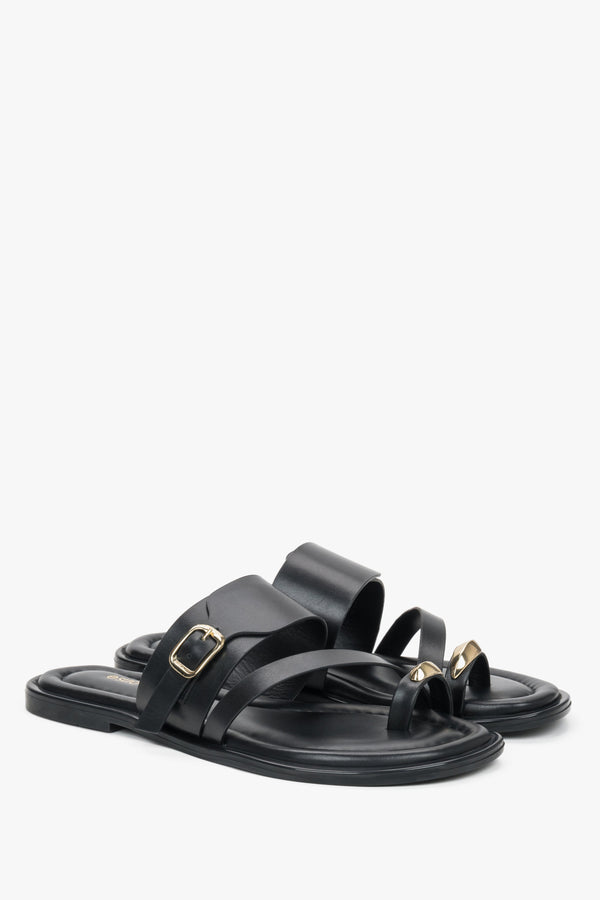 Black leather Estro mules with a toe loop, showcasing an asymmetrical upper line and a bold gold buckle detail.