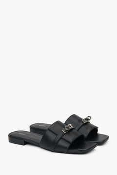 Elegant black Estro women's slide sandals, adorned with a silver embellishment, perfect for everyday wear, featuring a comfortable flat heel.