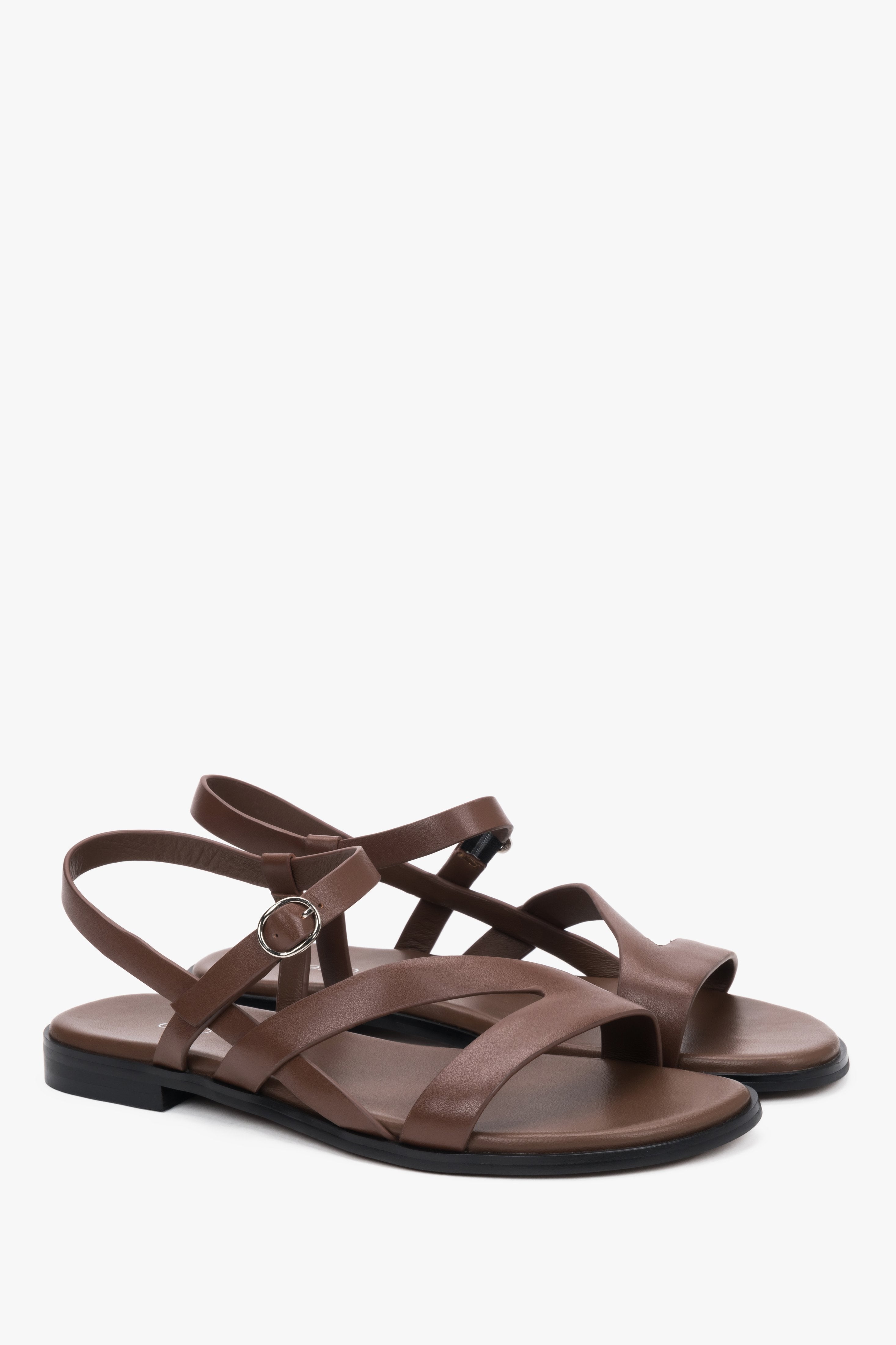 Brown women’s leather sandals with crisscross straps and a flat sole.