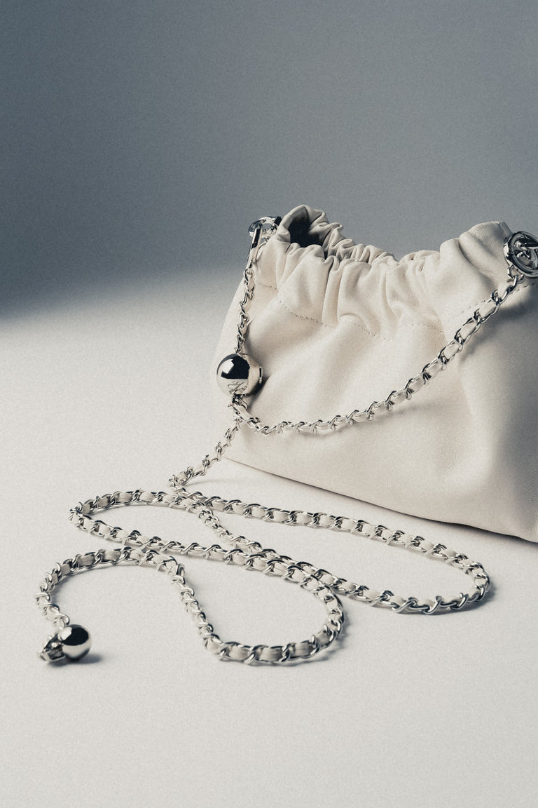 Detail view of silver chain strap on cream beige leather shoulder bag
