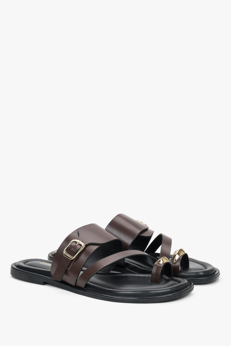 Dark brown leather Estro mules with a toe loop, showcasing an asymmetrical upper line and a bold gold buckle detail.