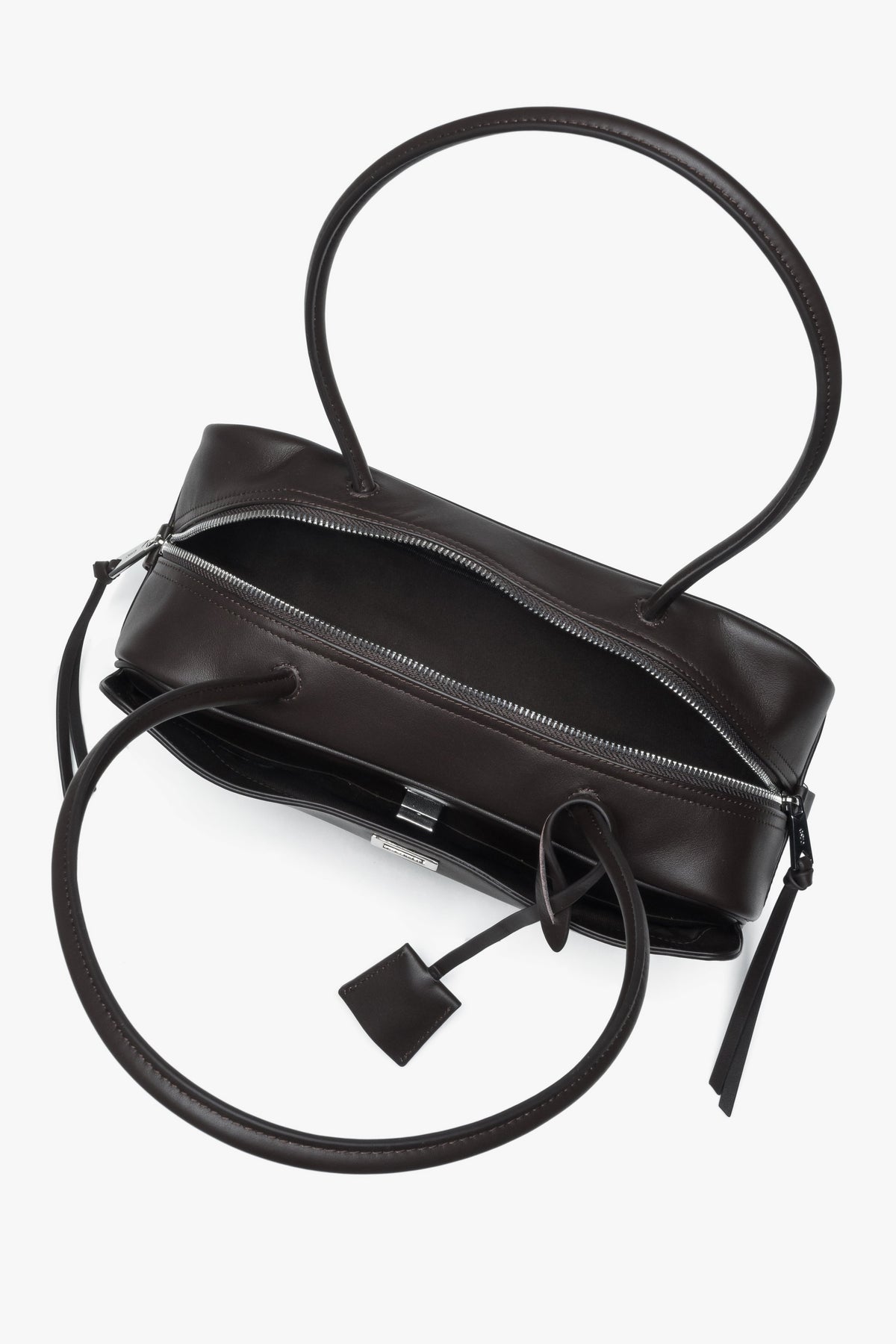 Elongated dark brown shoulder bag. Compact natural leather silhouette with a decorative bag charm.