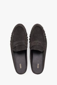 A pair of mules displayed to highlight the loafer-style closed front with a decorative cross strap and a sleek, dark-colored insole.