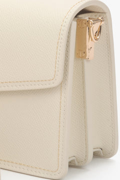 Compact off-white leather bag with a functional zipper and adjustable shoulder strap.