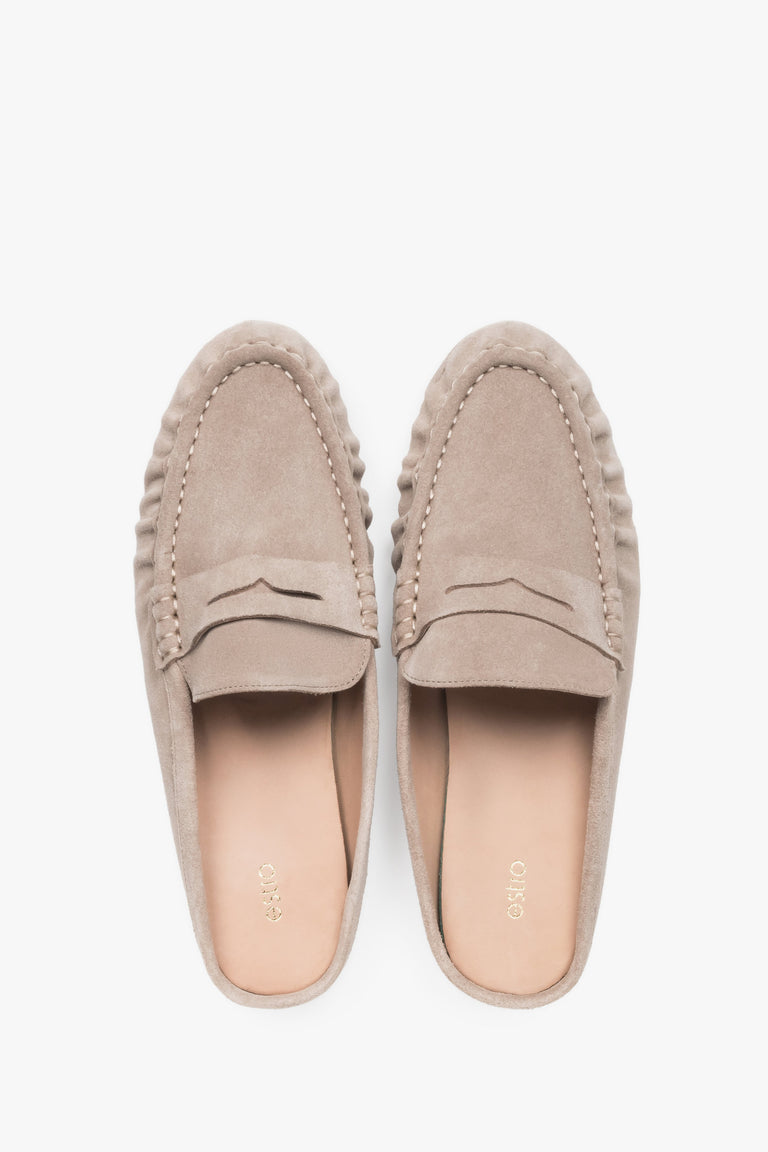 Top view of a pair of backless mules, showcasing a closed moccasin-style toe with a horizontal strap and a light leather insole.