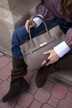 Women's brown leather handbag Estro - close-up view held by the model highlighting the polished hardware and leather texture.
