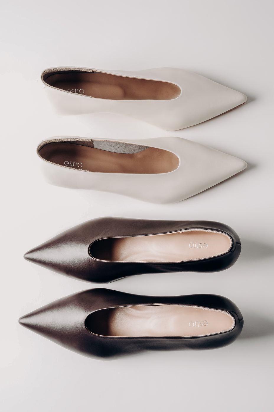 Four pairs of pointed-toe shoes in white, beige, and black on a light gray background.