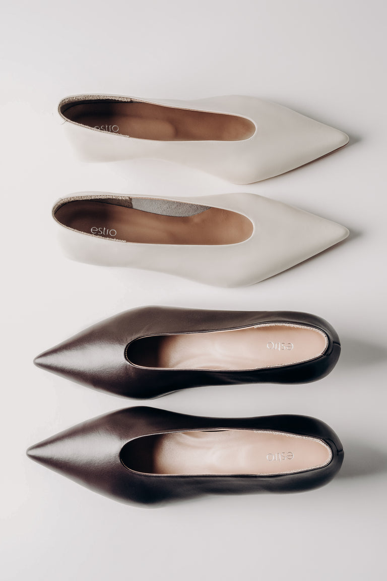 Four pairs of pointed-toe shoes in white, beige, and black on a light gray background.