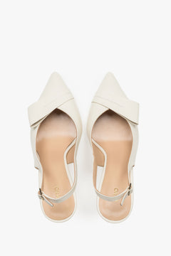 Top view of a pair of light beige pumps, showcasing a sharp pointed toe, an applied leather buckle detail, and a smooth insole featuring the brand logo.
