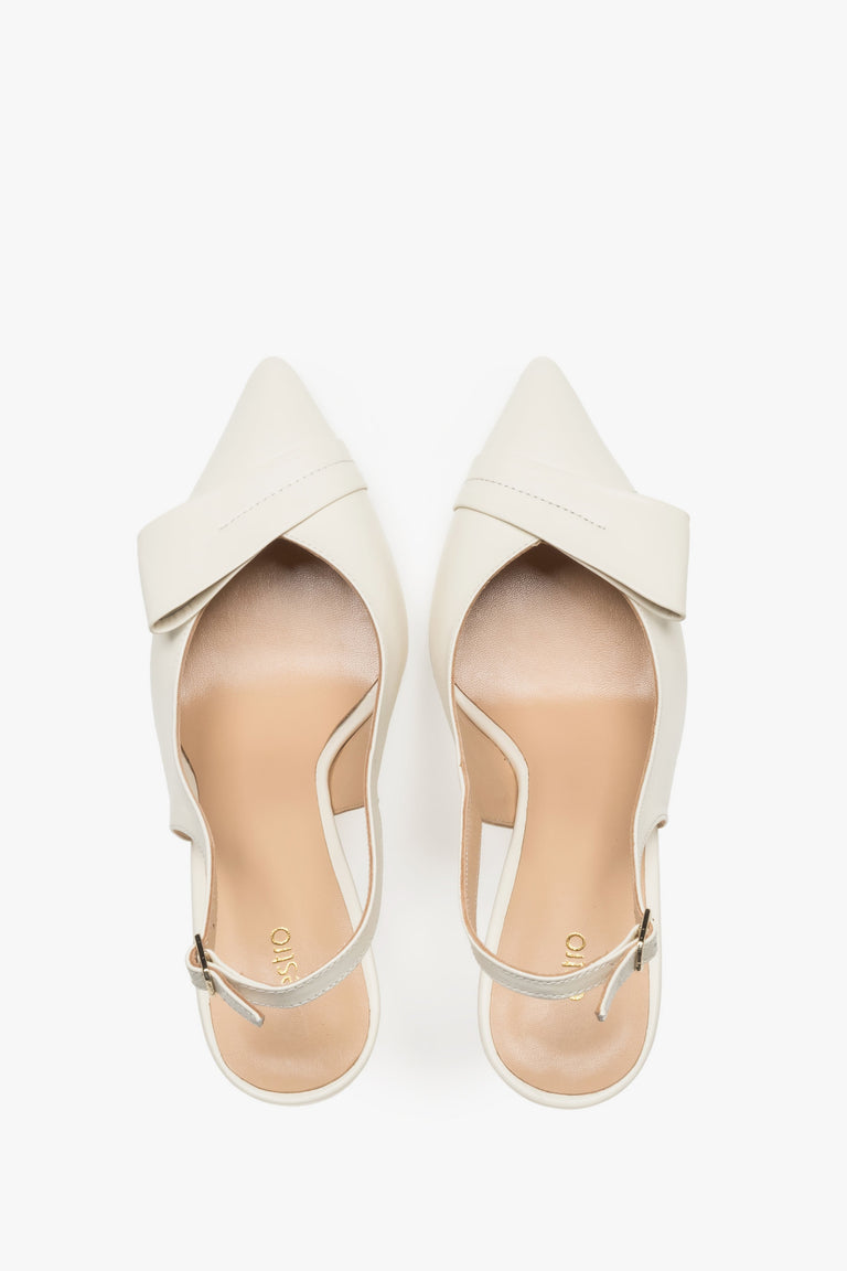 Top view of a pair of light beige pumps, showcasing a sharp pointed toe, an applied leather buckle detail, and a smooth insole featuring the brand logo.