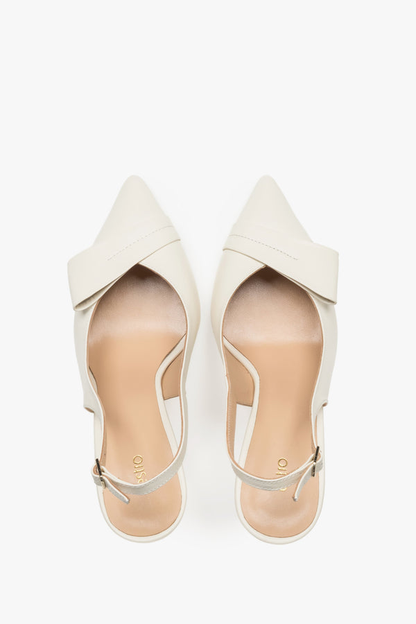 Top view of a pair of light beige pumps, showcasing a sharp pointed toe, an applied leather buckle detail, and a smooth insole featuring the brand logo.