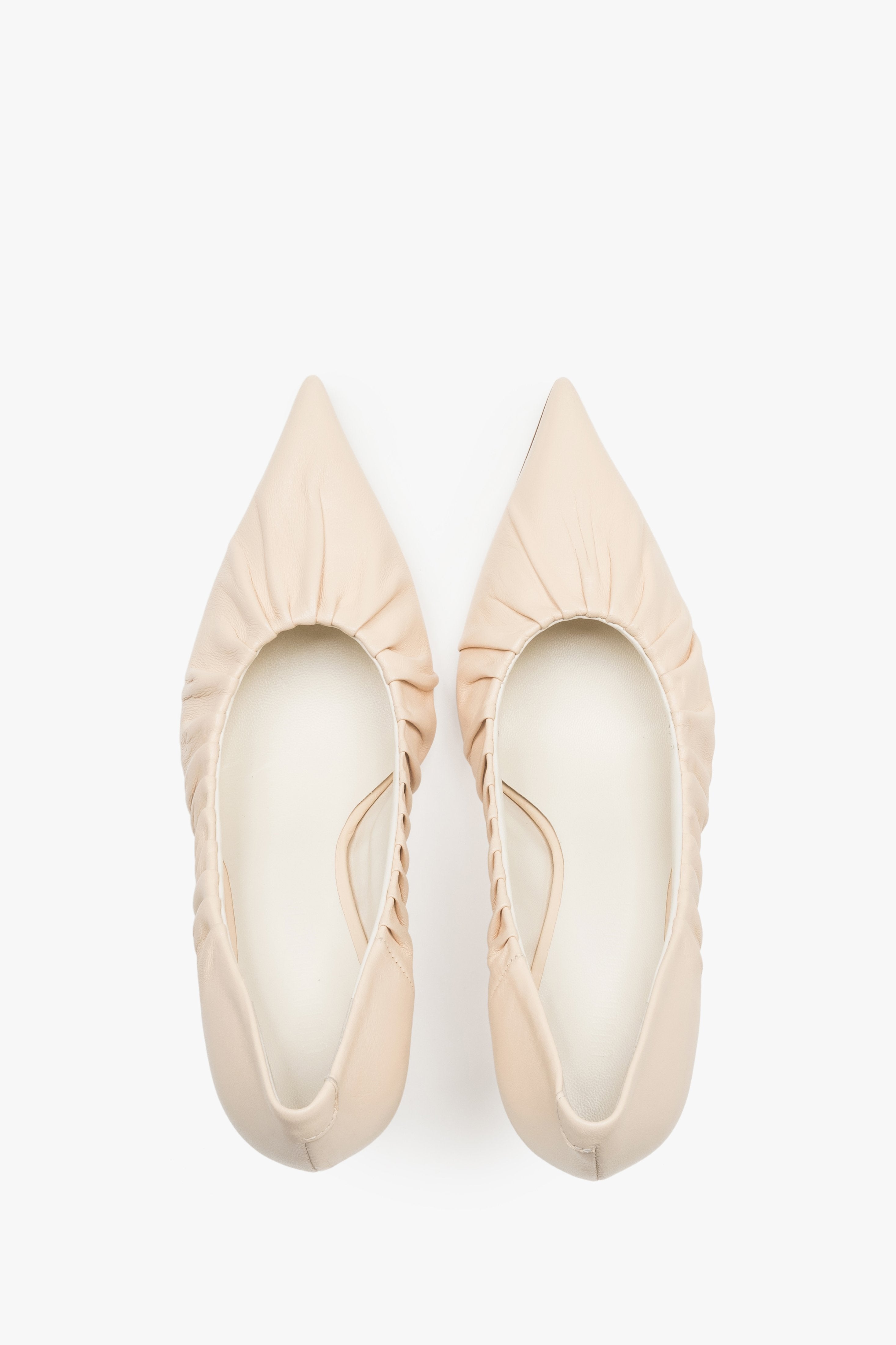 Close-up of the artistic gathered leather topline and pointed-toe design on beige pumps.