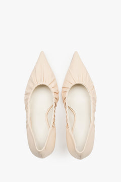 Close-up of the artistic gathered leather topline and pointed-toe design on beige pumps.