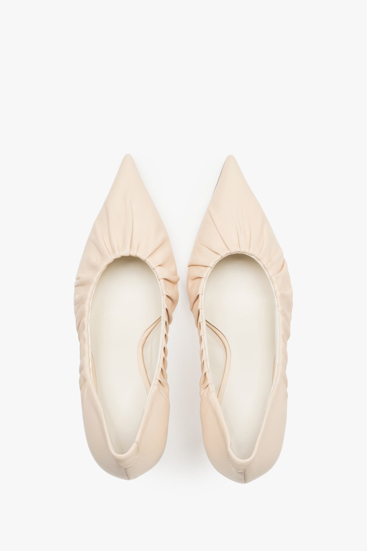 Close-up of the artistic gathered leather topline and pointed-toe design on beige pumps.