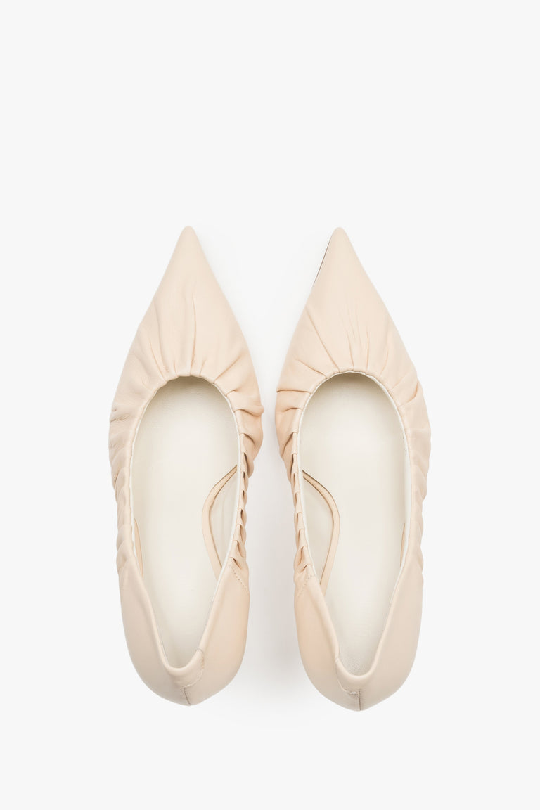 Close-up of the artistic gathered leather topline and pointed-toe design on beige pumps.