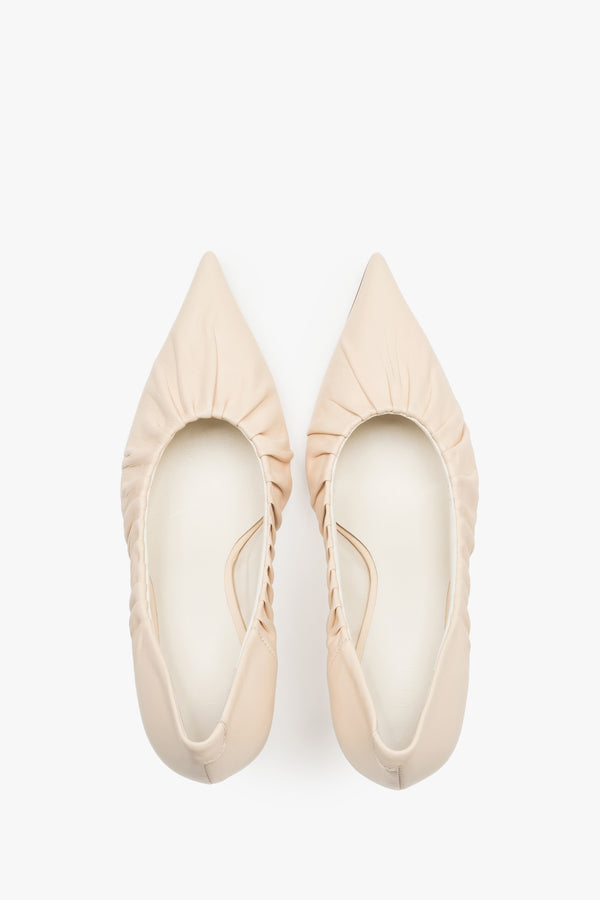 Close-up of the artistic gathered leather topline and pointed-toe design on beige pumps.