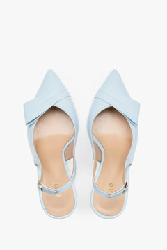 Top view of a pair of light blue pumps, showcasing a sharp pointed toe, an applied leather buckle detail, and a smooth natural leather insole featuring the brand logo.