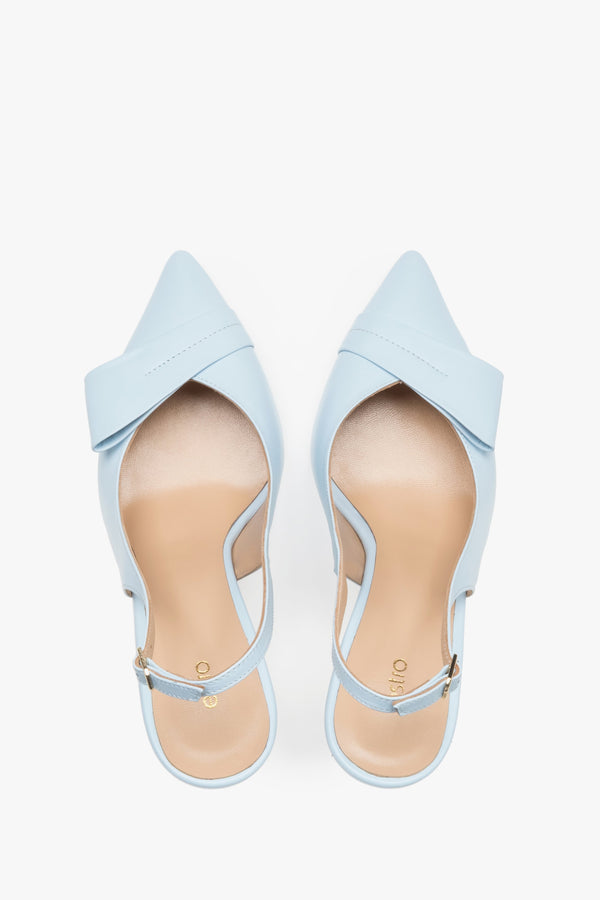 Top view of a pair of light blue pumps, showcasing a sharp pointed toe, an applied leather buckle detail, and a smooth natural leather insole featuring the brand logo.