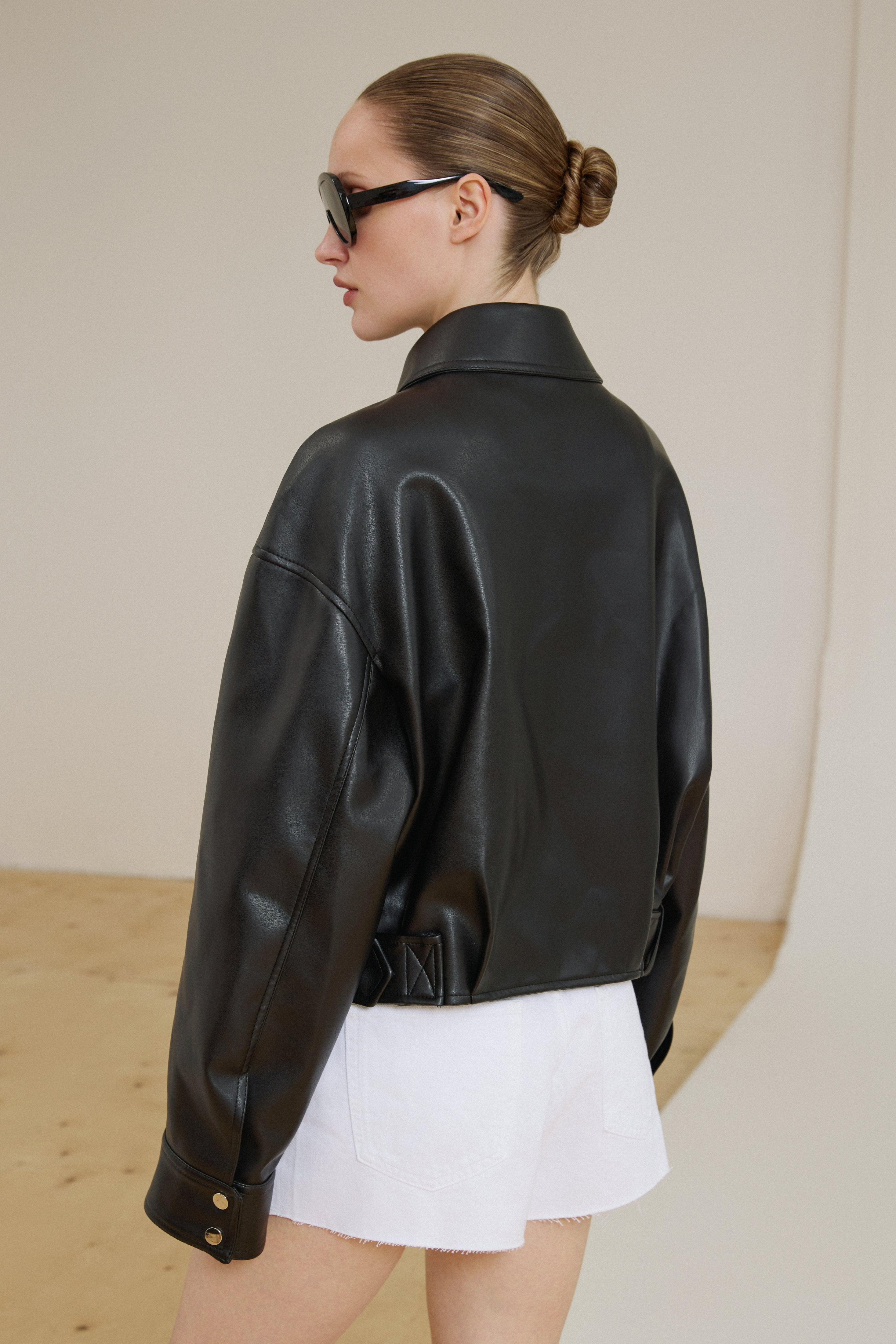 Short faux leather jacket with dropped shoulders, showcasing the loose cut of the sleeves and an above-the-hip length.