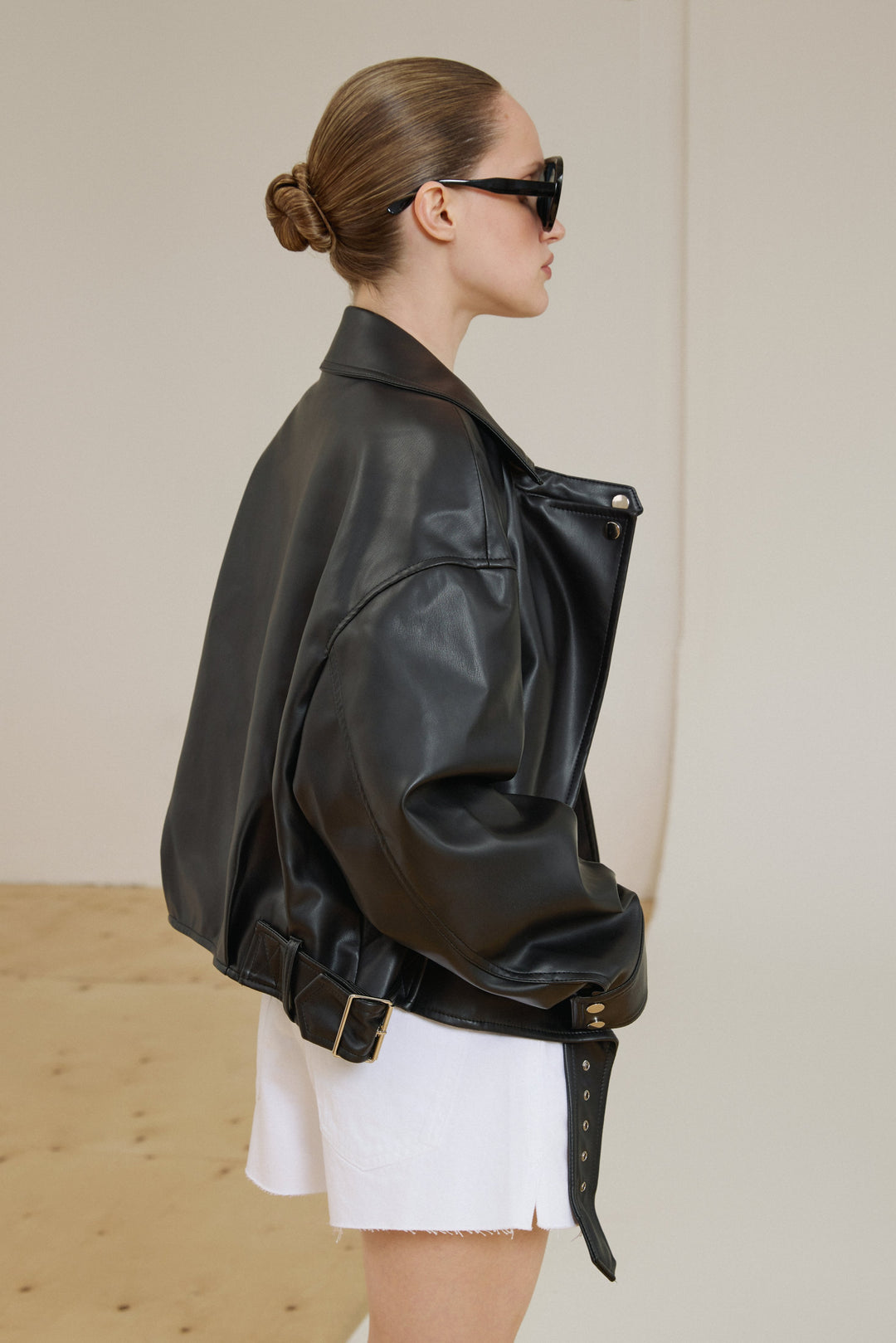 The back of the jacket displaying the smooth, uniform texture of the black faux leather and a loose, oversized bomber-style profile.
