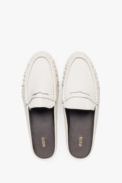 View of a pair of mules showcasing a distinctive moccasin-style toe with a cross strap and a contrasting black natural leather insole.