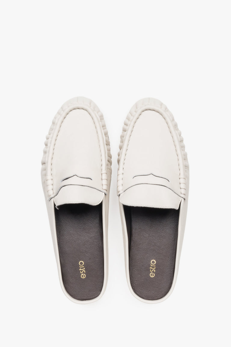 View of a pair of mules showcasing a distinctive moccasin-style toe with a cross strap and a contrasting black natural leather insole.