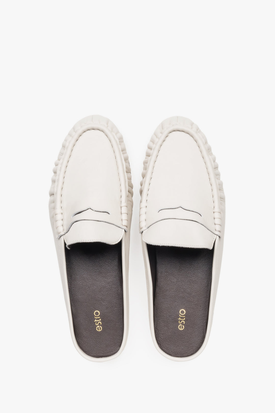 View of a pair of mules showcasing a distinctive moccasin-style toe with a cross strap and a contrasting black natural leather insole.