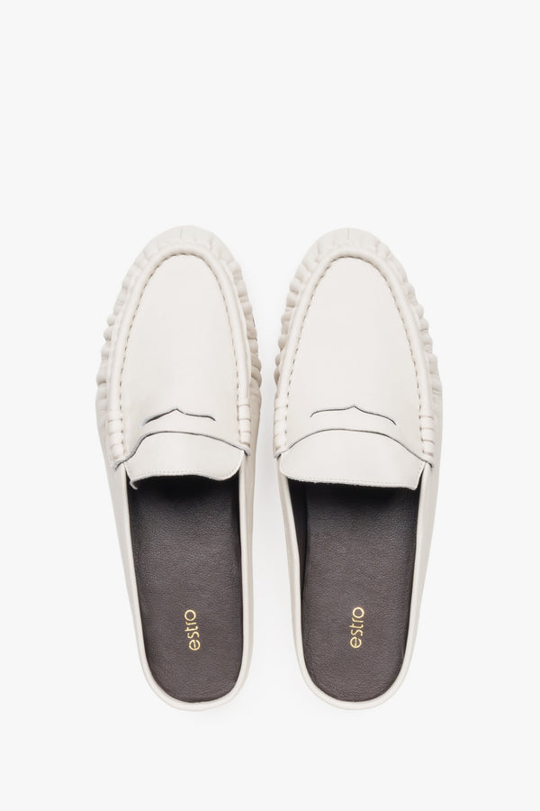 View of a pair of mules showcasing a distinctive moccasin-style toe with a cross strap and a contrasting black natural leather insole.