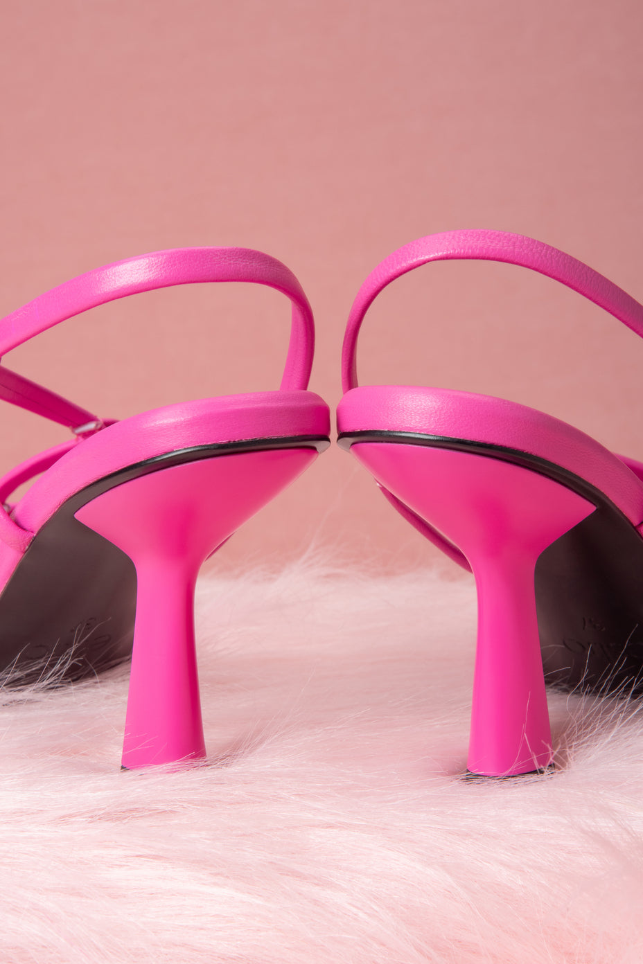 Pink high-heeled shoes on a pink fur surface with a pink background.