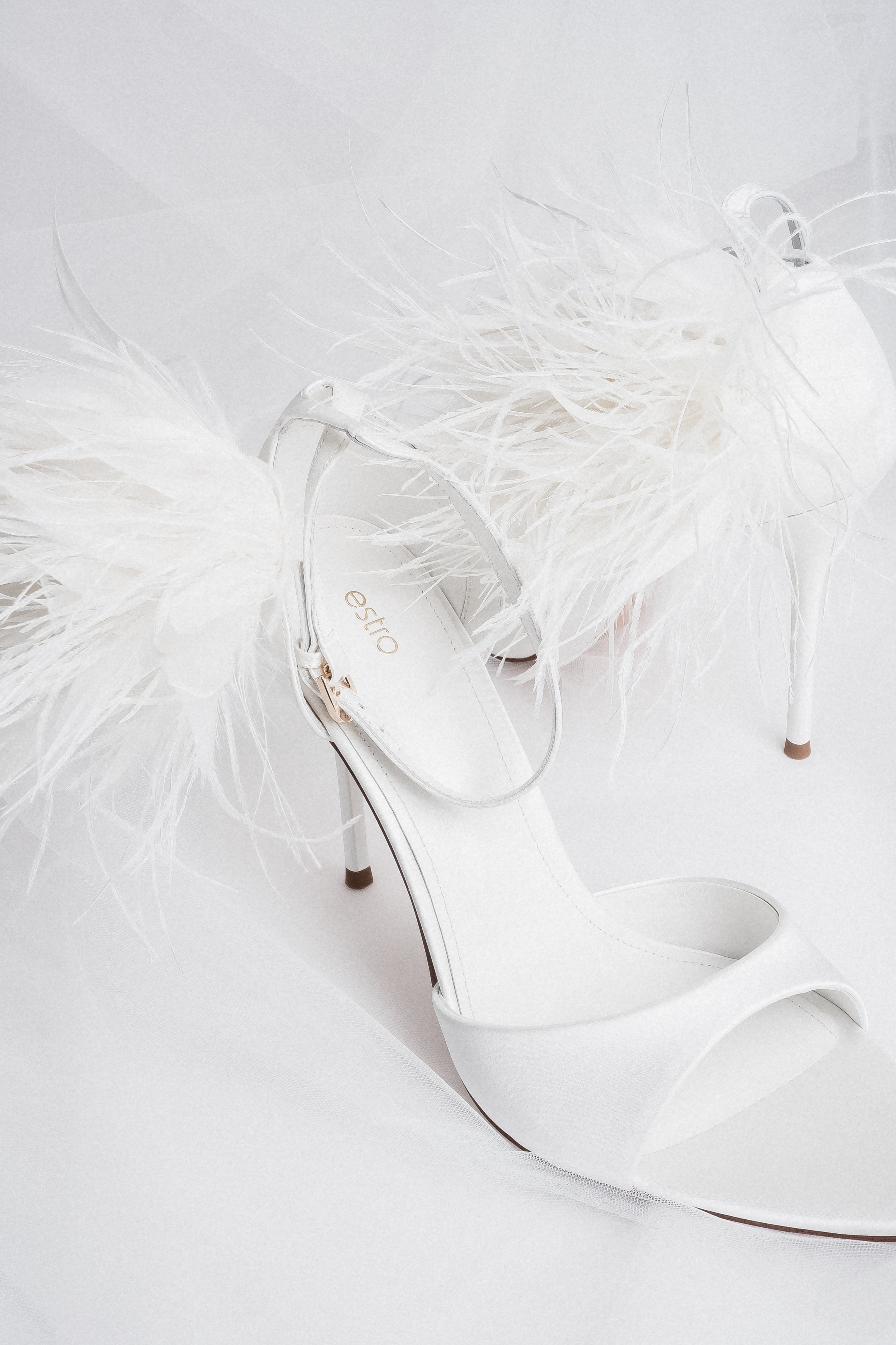 Detail view of buckle and feather trim on white high heel sandals