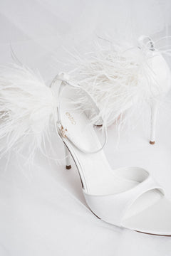 Detail view of buckle and feather trim on white high heel sandals